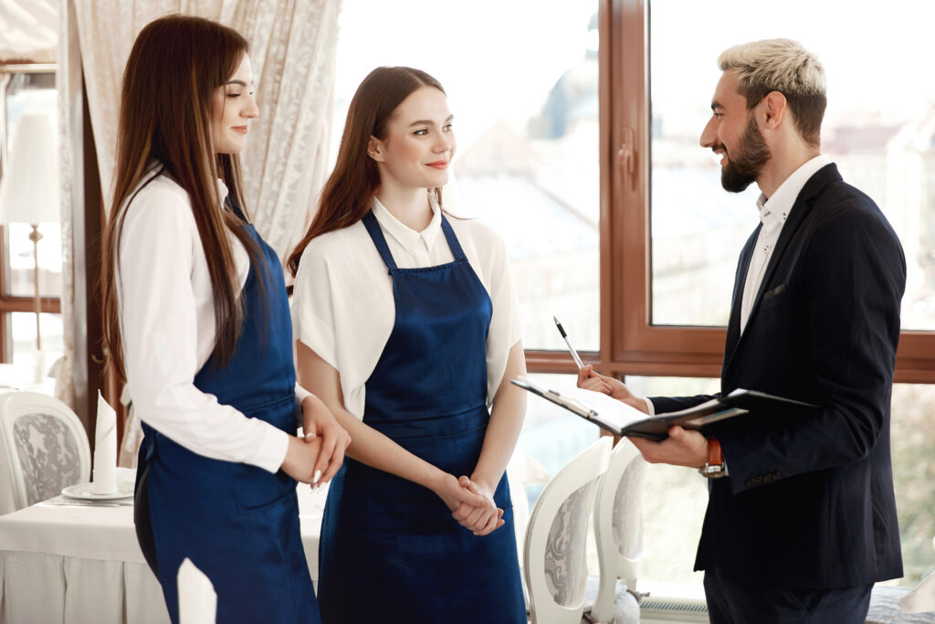 Handsome restaurant manager is talking to waitresses about work